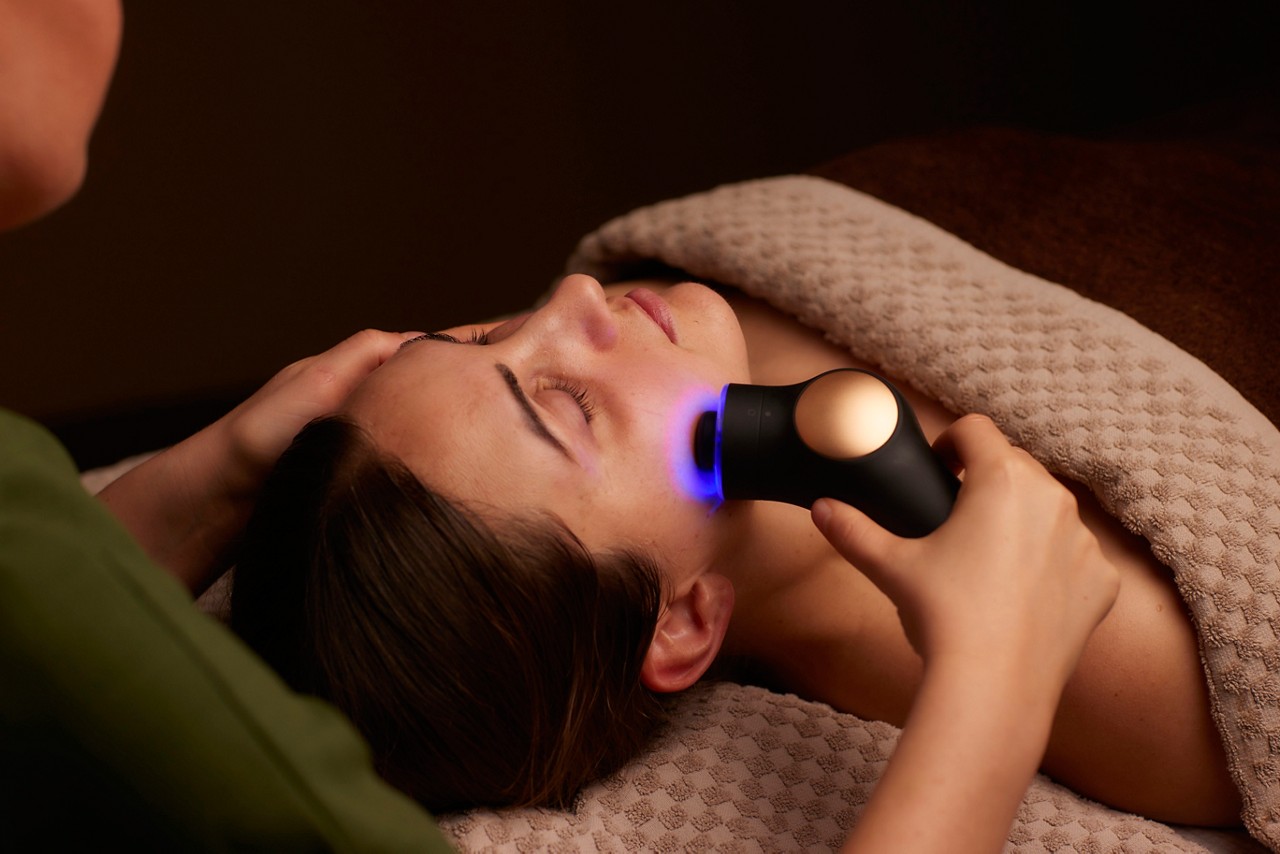 Spa therapist giving a woman a Theraface microcurrent facial treatment.